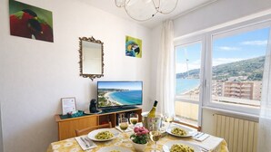 A dining area with a table set for four, a television, and a scenic view of the sea. - Fronte mare con terrazza e garage (Marina di Andora)