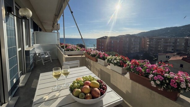 A balcony with a table set with fruit and wine glasses, overlooking a cityscape and the sea. - Fronte mare con terrazza e garage (Marina di Andora)