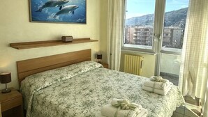 A hotel room with a bed, a painting of dolphins, a window with a city view, and a chandelier. - Fronte mare con terrazza e garage (Marina di Andora)