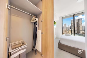 Ein Hotelzimmer mit Bett, Blick auf die Stadt, einer Holztür und einem Schrank mit Kleidung.