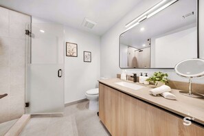 Un baño moderno con cabina de ducha de vidrio, inodoro, lavamanos con espejo y una planta en maceta.