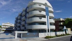 A multi-story building with a modern architectural design, featuring balconies and a central vertical element. - Inviting Apartment Close to the Beach in Grado (Grado)
