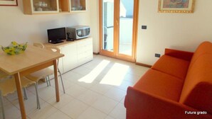 A compact living space with a dining area, kitchenette, and a sliding glass door leading to a balcony. - Inviting Apartment Close to the Beach in Grado (Grado)