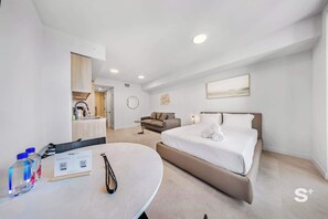 A modern hotel room with a bed, a sofa, a dining table with water bottles, and a kitchen area in the background. - Spacious Studio | Rooftop Pool & Gym | 29th Floor (Miami)