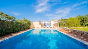 A swimming pool with a stone border, surrounded by greenery and a clear sky. - Vivenda Liberdade in Carvoeiro (Lagoa)