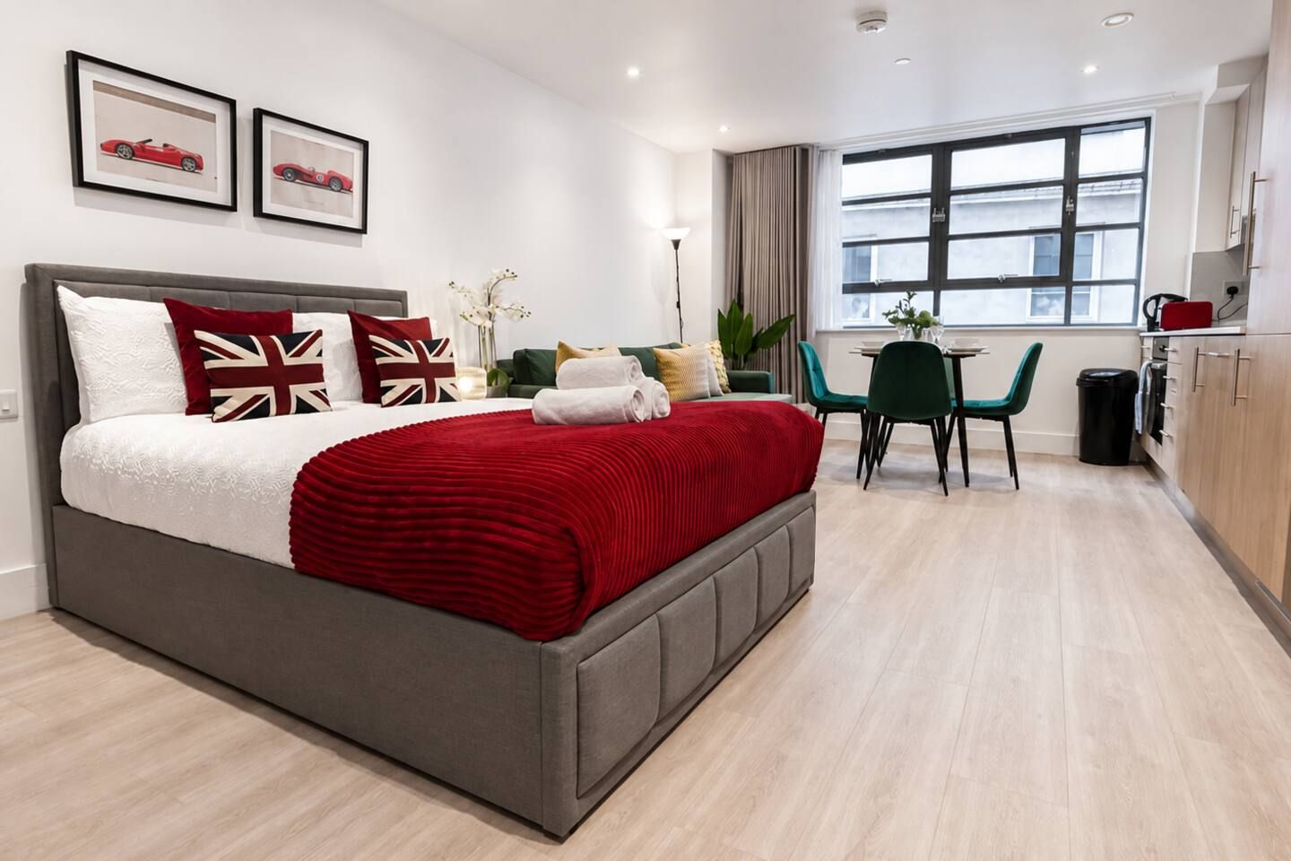 Una camera d'albergo moderna con un letto grande, un'area ristoro con tavolo e sedie, e vista sulla città dalla finestra.