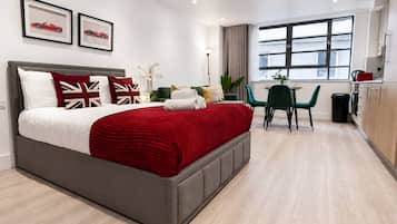 Una camera d'albergo moderna con un letto grande, un'area ristoro con tavolo e sedie, e vista sulla città dalla finestra.