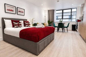 A modern hotel room with a large bed, a dining area with a table and chairs, and a view of the city through the window. - Furnished Studio Apt Near Regent's park + ac/lift (London)