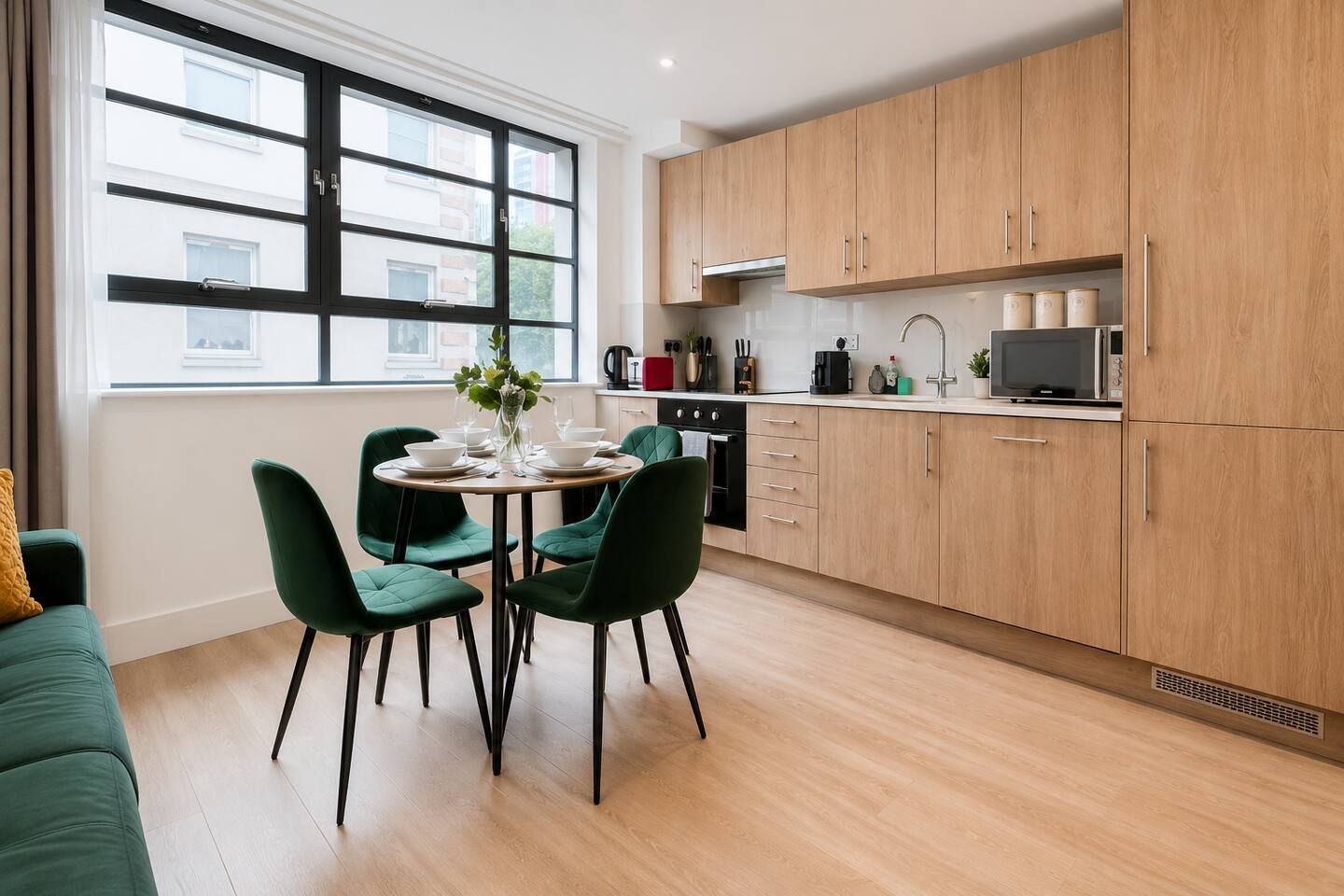 A modern kitchen with wooden cabinets, a dining table with chairs, and a window with a view of buildings.