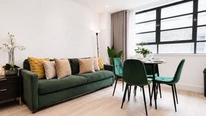 Una sala moderna con un sofá verde, sillas a juego, una mesa de comedor y un ventanal con cortinas.