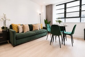 Un salon moderne avec un canapé vert, des fauteuils assortis, une table à manger et une grande fenêtre avec des rideaux.