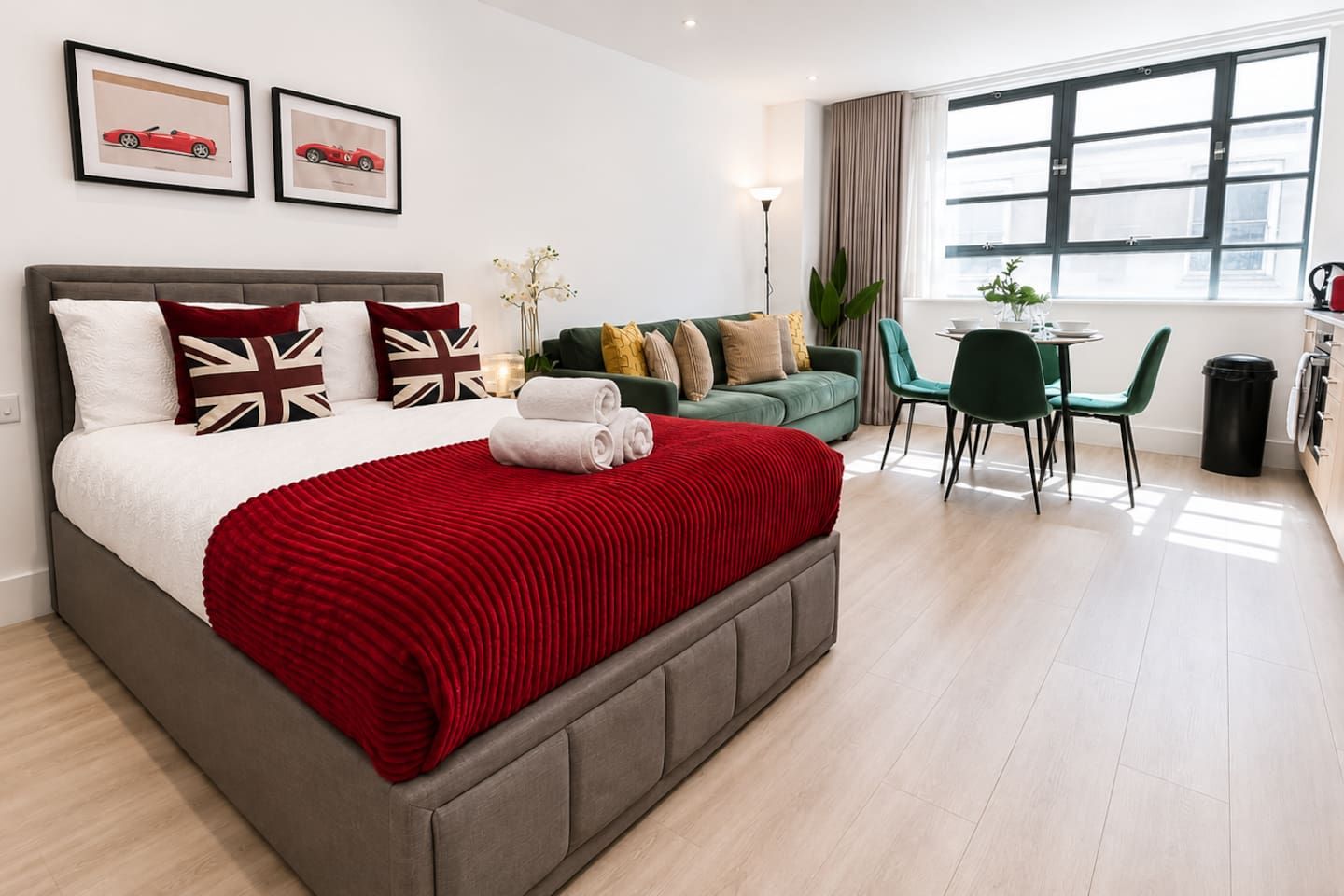 Una camera d'albergo con un letto, un divano verde, un tavolo da pranzo con sedie e una finestra con tende.