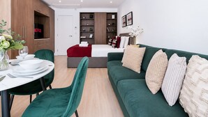 Uma sala de estar moderna com um sofá verde, uma mesa de jantar com cadeiras, uma televisão e uma estante de livros.