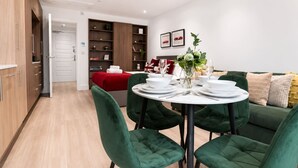 Una sala de estar moderna con una mesa de comedor redonda dispuesta para cuatro personas, sillas tapizadas de verde, un sofá rojo y una estantería.