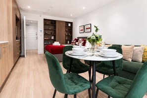 A modern living room with a round dining table set for four, green upholstered chairs, a red sofa, and a bookshelf. - Furnished Studio Apt Near Regent's park + ac/lift (London)