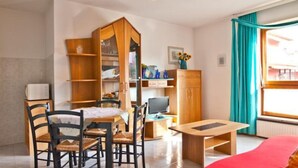 A compact living space with a dining area, a television, and a window with curtains. - Cozy Flat for Four Guests Just Steps From the sea (Grado)