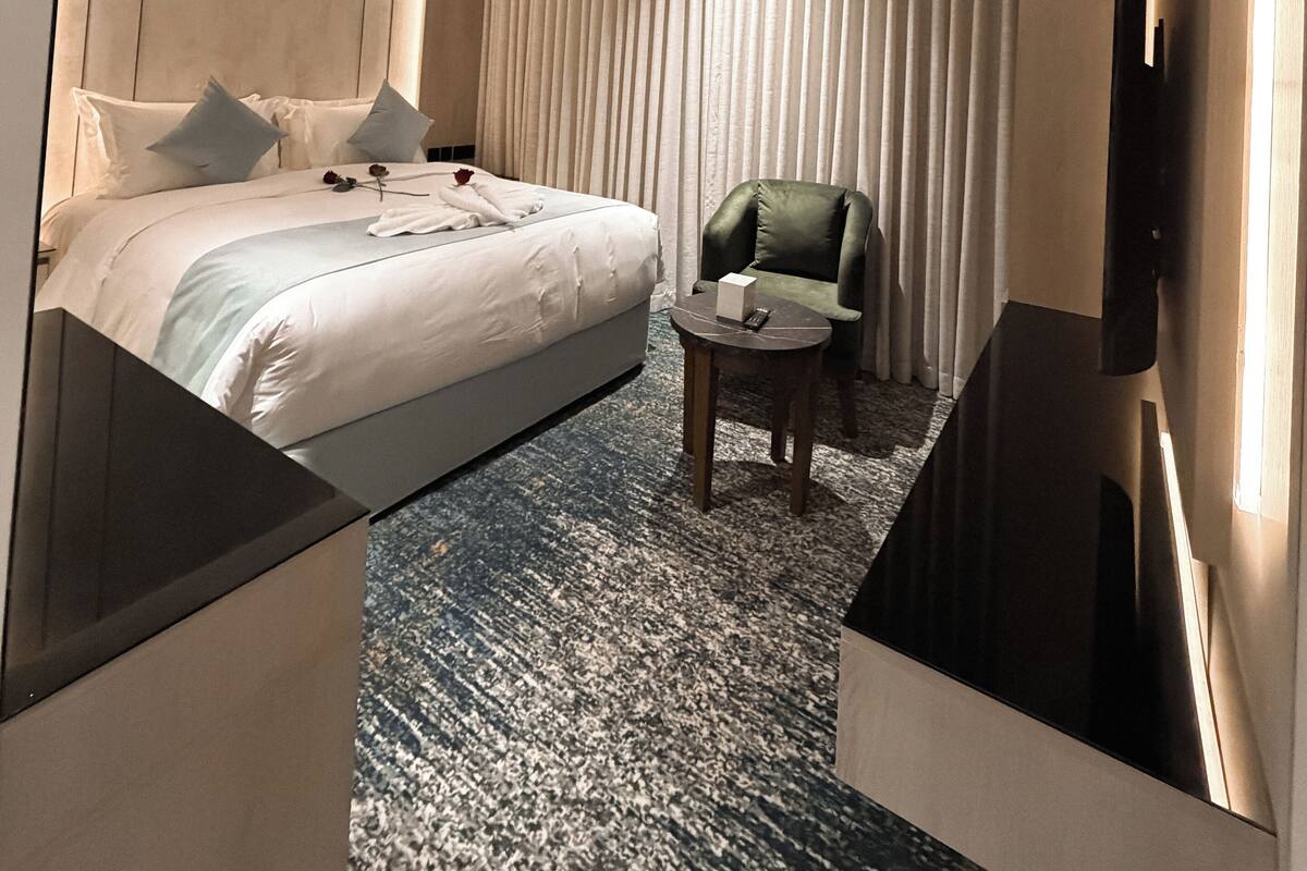 A modern hotel room with a large bed, a green armchair, a small table, and a flat-screen TV.