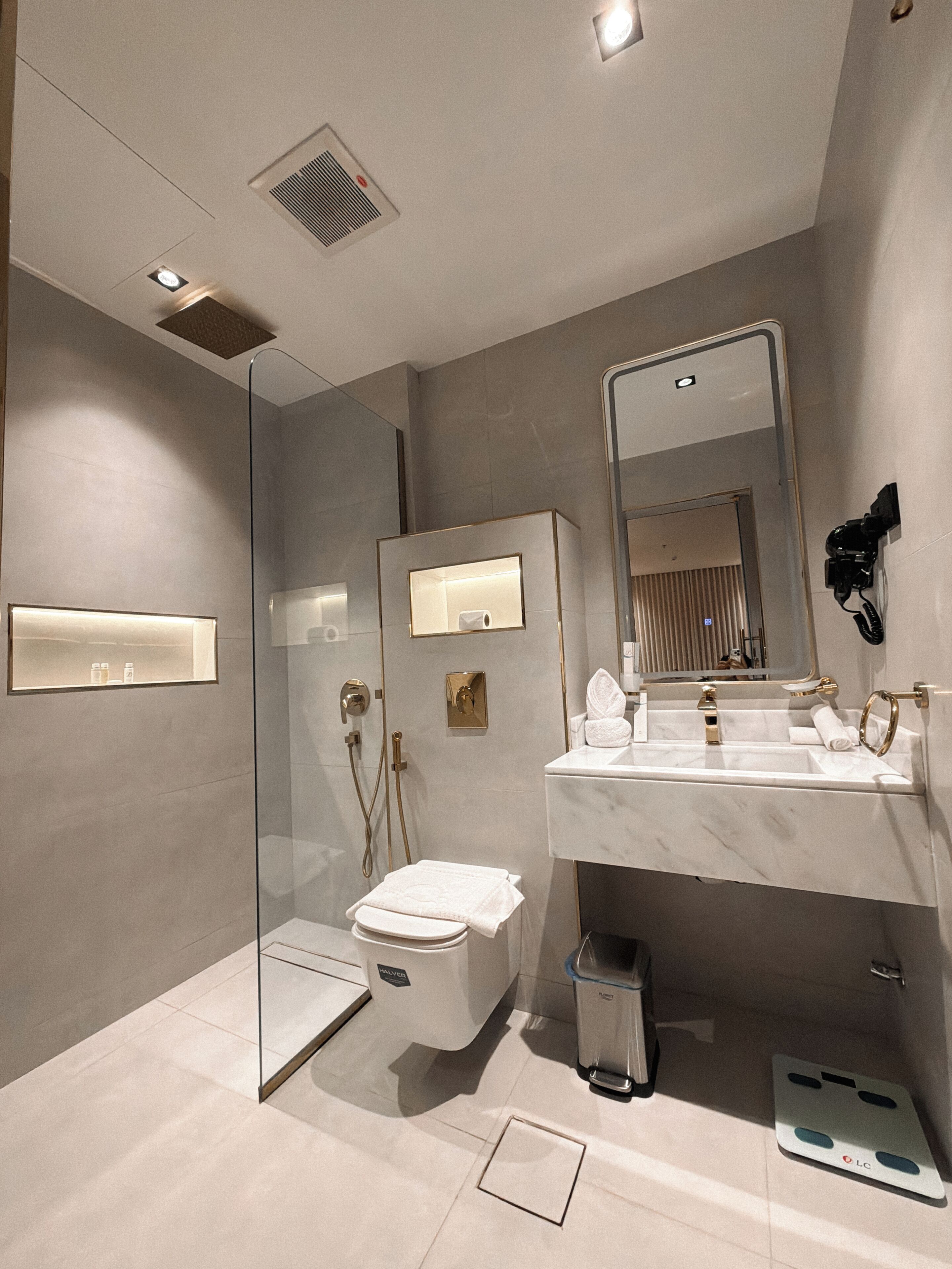 A modern bathroom with a glass-enclosed shower, a toilet, a sink with a mirror, and a trash bin.