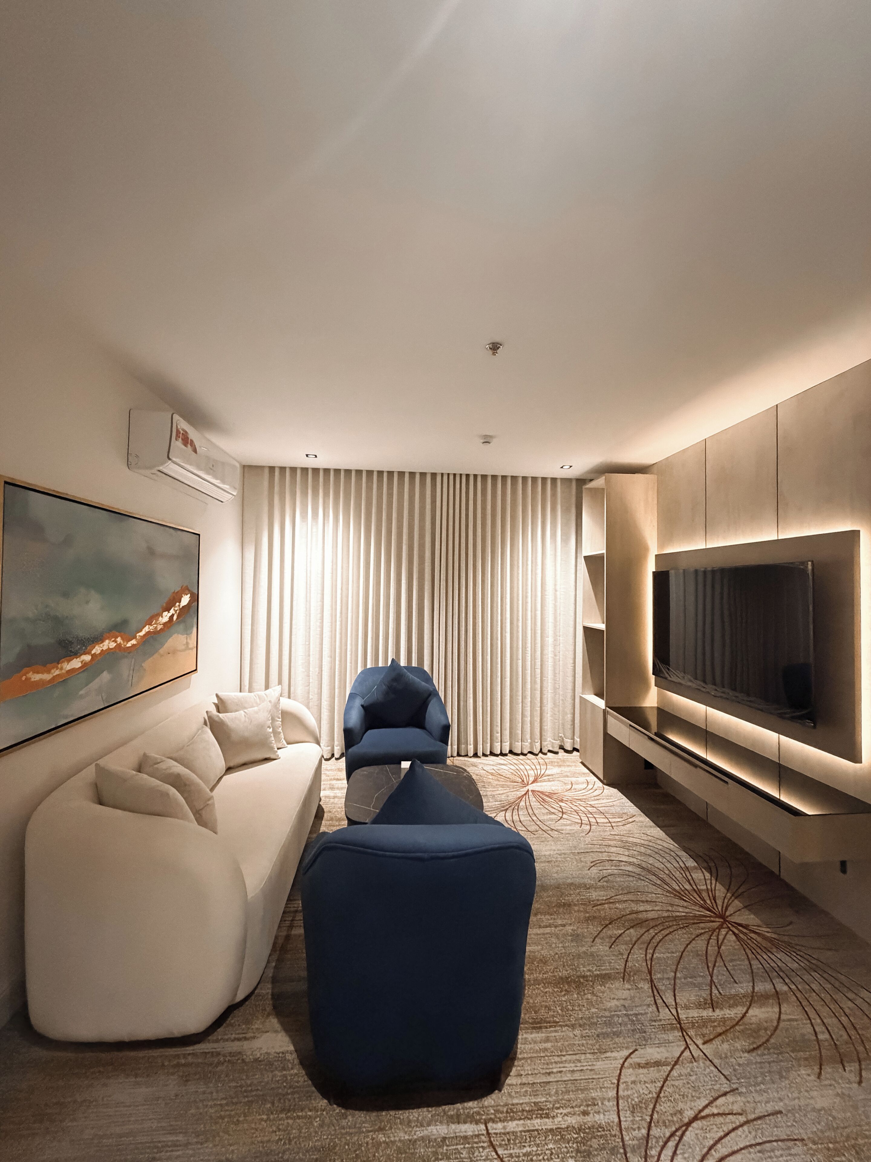 A modern hotel room with a sofa, armchair, and TV.