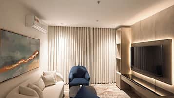 A modern hotel room with a sofa, armchair, and TV.