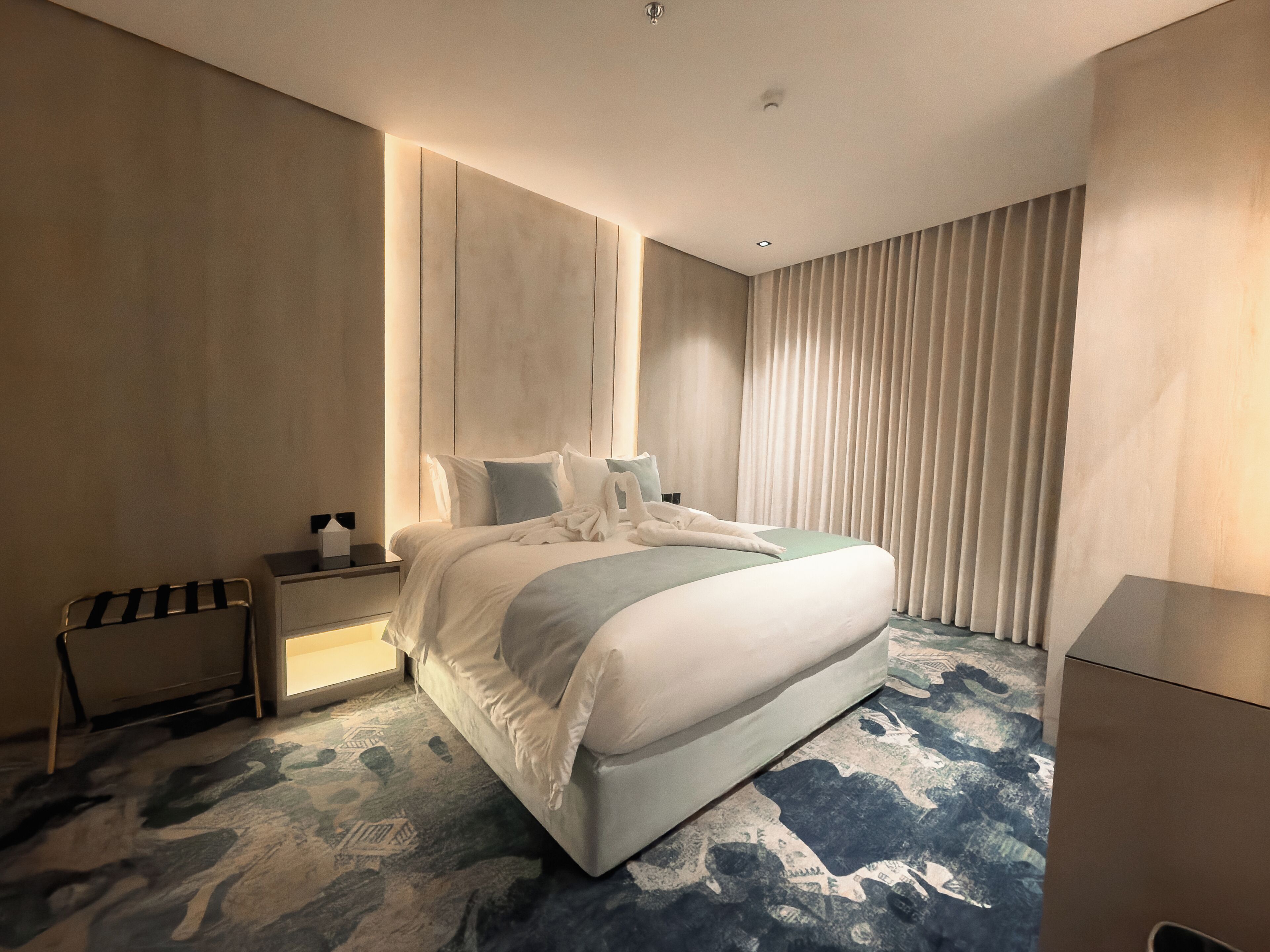 A modern hotel room with a large bed, bedside tables, and a patterned carpet.