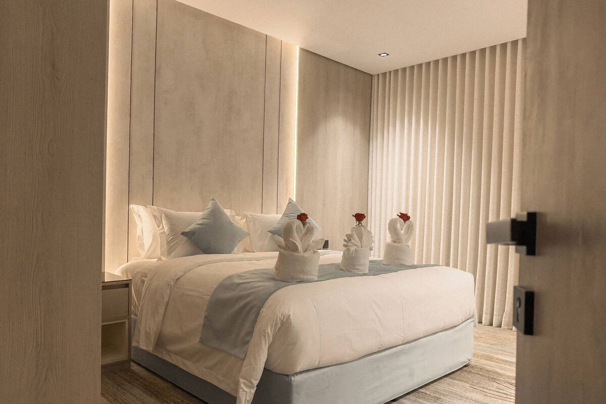 A modern bedroom with a large bed, white bedding, and rose-shaped bathrobes on the bed.