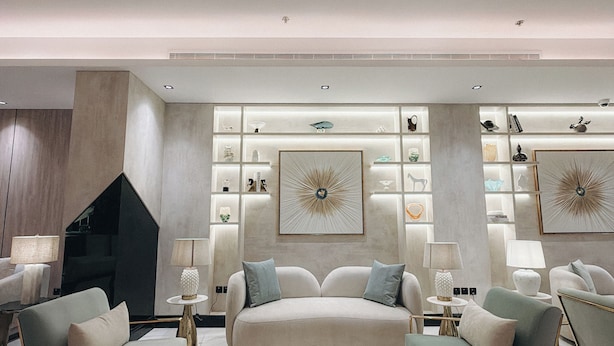 Un soggiorno moderno con un ampio divano color beige, due poltrone, un tavolino in marmo e decorazioni murali.