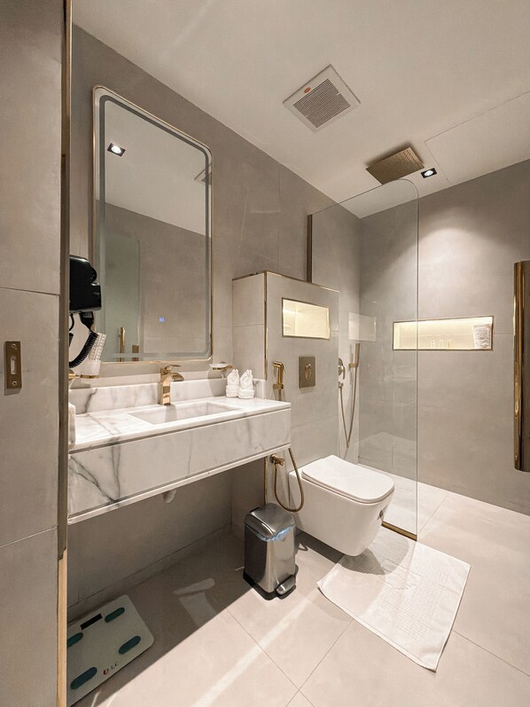 A modern bathroom with a large mirror, dual sinks, a toilet, and a shower area. - Rose Garden Hotel Riyadh (Riyadh)
