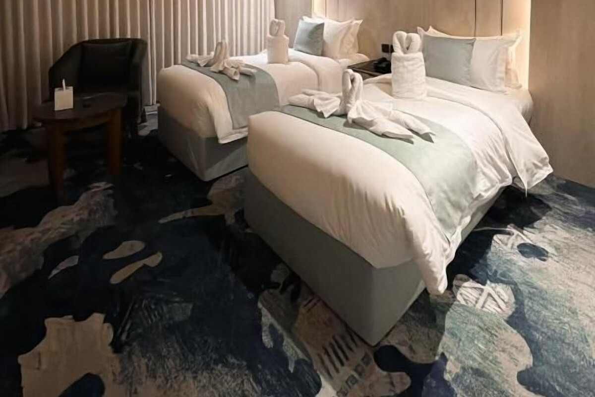Habitación de hotel con dos camas, zona de estar y un amplio ventanal.