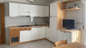 A modern kitchen with white cabinets, a wooden countertop, a built-in TV, and a dining area with a table and chairs. - Sea Breeze Holiday Villa in Grado (Grado)