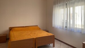 A bedroom with a wooden bed, a nightstand, and a window with sheer curtains. - Sea Breeze Holiday Villa in Grado (Grado)