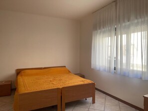 A bedroom with a wooden bed, a nightstand, and a window with sheer curtains. - Sea Breeze Holiday Villa in Grado (Grado)