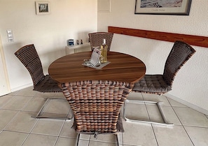A round wooden table with a woven chair in the center, a bottle of wine, and a menu on the table. - Vacation apartment Deichbrise within walking distance of the beach and harbor (Wurster Nordseeküste)