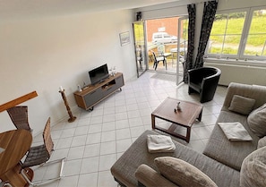 A modern living room with a sofa, a coffee table, a TV on a stand, and a dining area with chairs and a table. - Vacation apartment Deichbrise within walking distance of the beach and harbor (Wurster Nordseeküste)