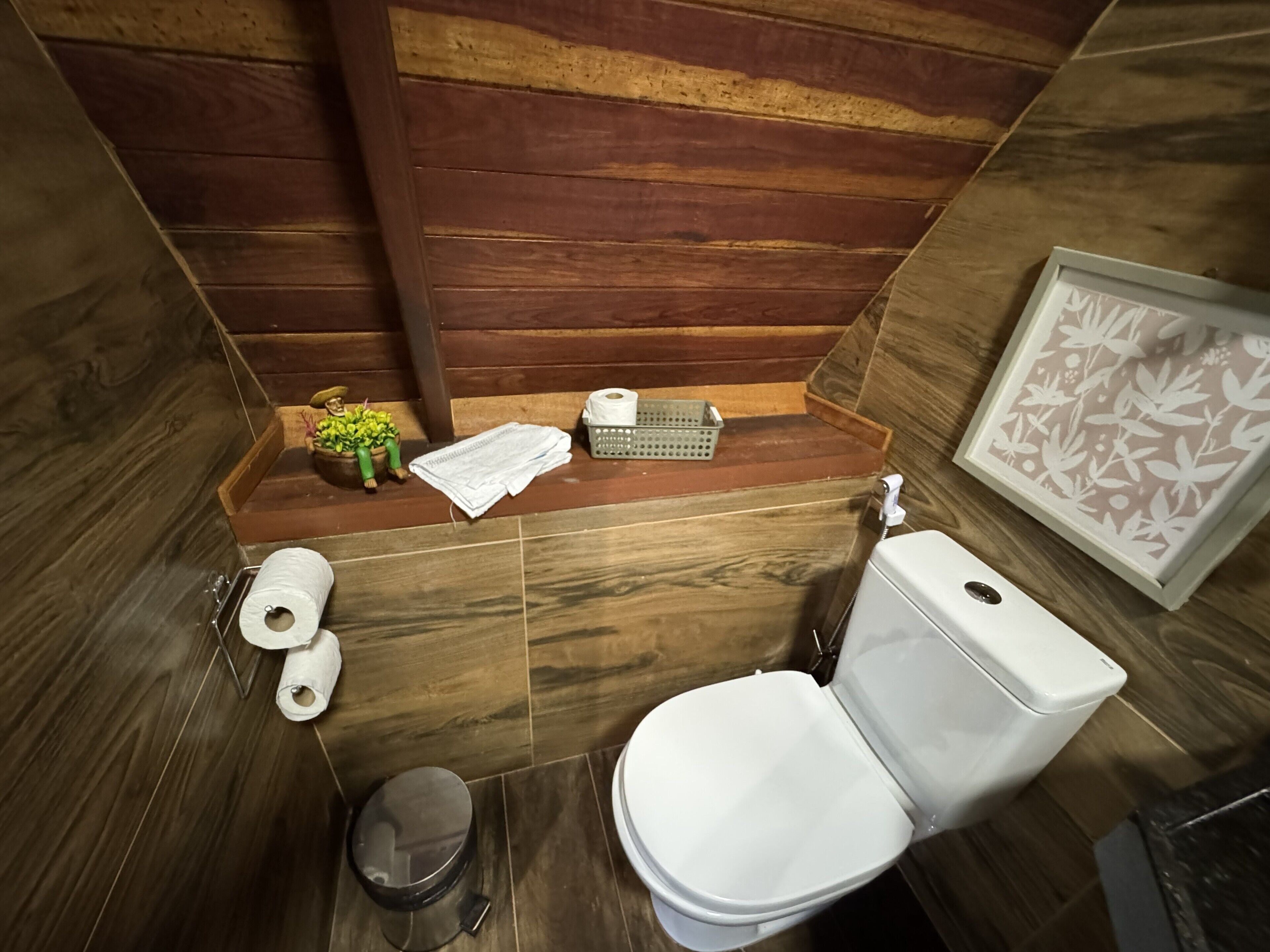 A compact bathroom with a toilet, a small trash bin, and a shelf with toiletries.