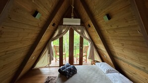 Une chambre confortable située dans les combles, avec un lit, un plancher en bois et une vue sur un patio extérieur aménagé avec des chaises.