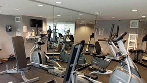 Un gimnasio con diversas máquinas de ejercicio, un espejo grande y un televisor en la pared.