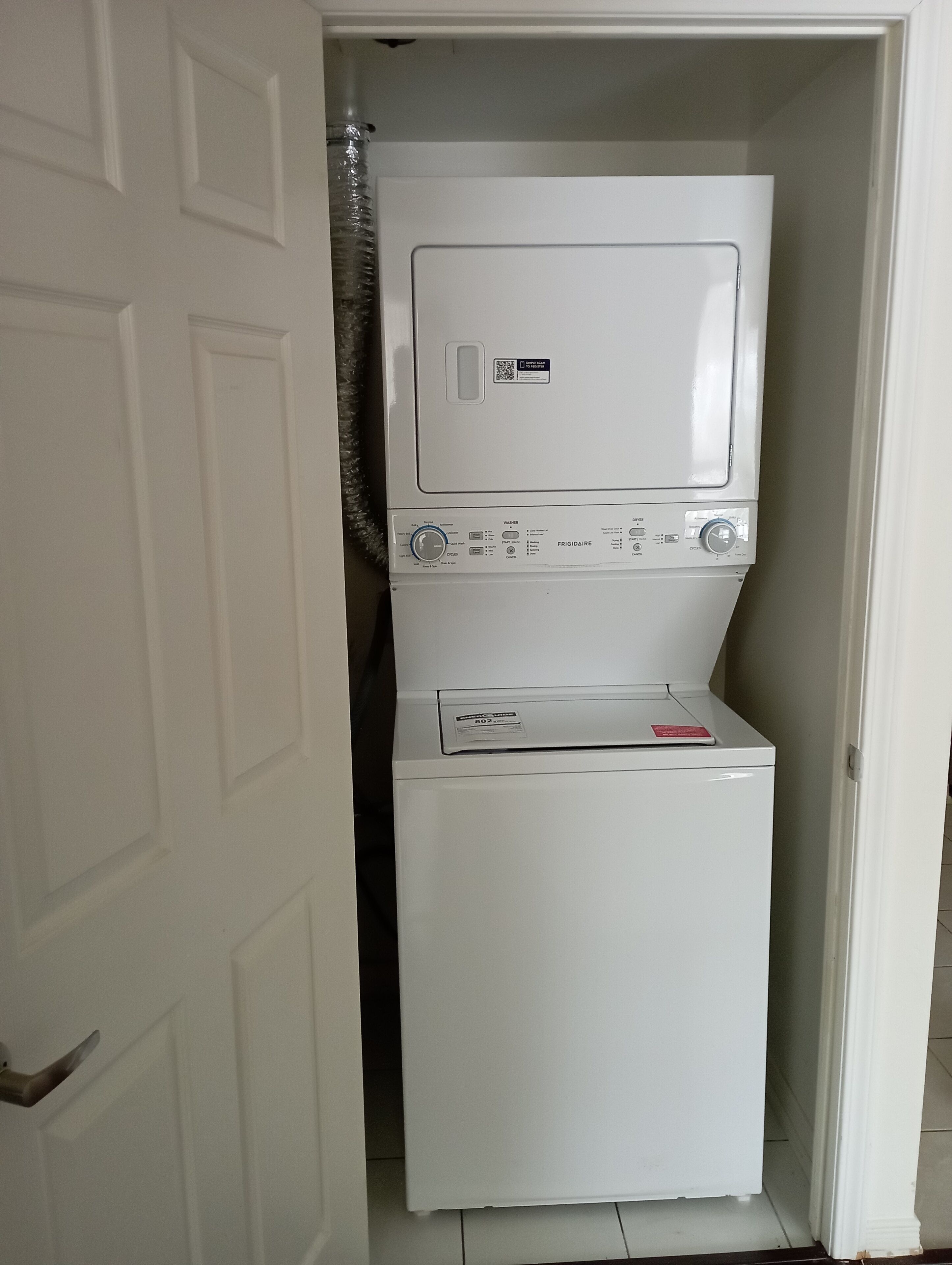 Une petite buanderie équipée d’un lave-linge et d’un sèche-linge à chargement frontal, d’une porte et d’une petite étagère.
