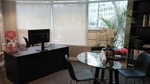 Una oficina moderna con un escritorio, computadora, sillas, una mesa de vidrio y un ventanal con vistas a edificios.