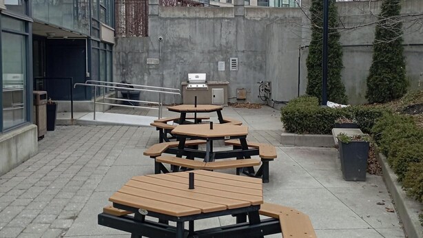Un patio con mobiliario exterior y zona de barbacoa, rodeado de edificios modernos.