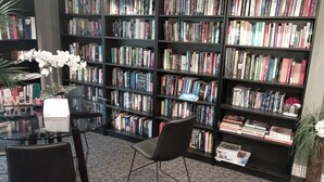 Una biblioteca con numerosas estanterías llenas de libros, una mesa de vidrio con sillas y una planta en maceta.