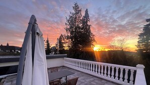 A patio with a table and chairs, a white railing, and a view of the sunset over trees. - Merzhausen Castle in the Taunus region near Frankfurt am Main - west wing (Usingen)