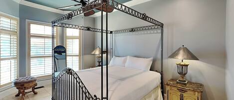 Una cama con dosel y cuatro columnas, un ventilador de techo, dos lámparas de noche y una mesita de madera.