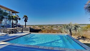 A swimming pool with a wooden deck, surrounded by palm trees and a view of the beach. - Legasea (Gulf Shores)