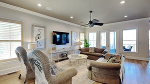 A spacious living room with a large flat-screen TV, comfortable seating, and a ceiling fan. - Legasea (Gulf Shores)