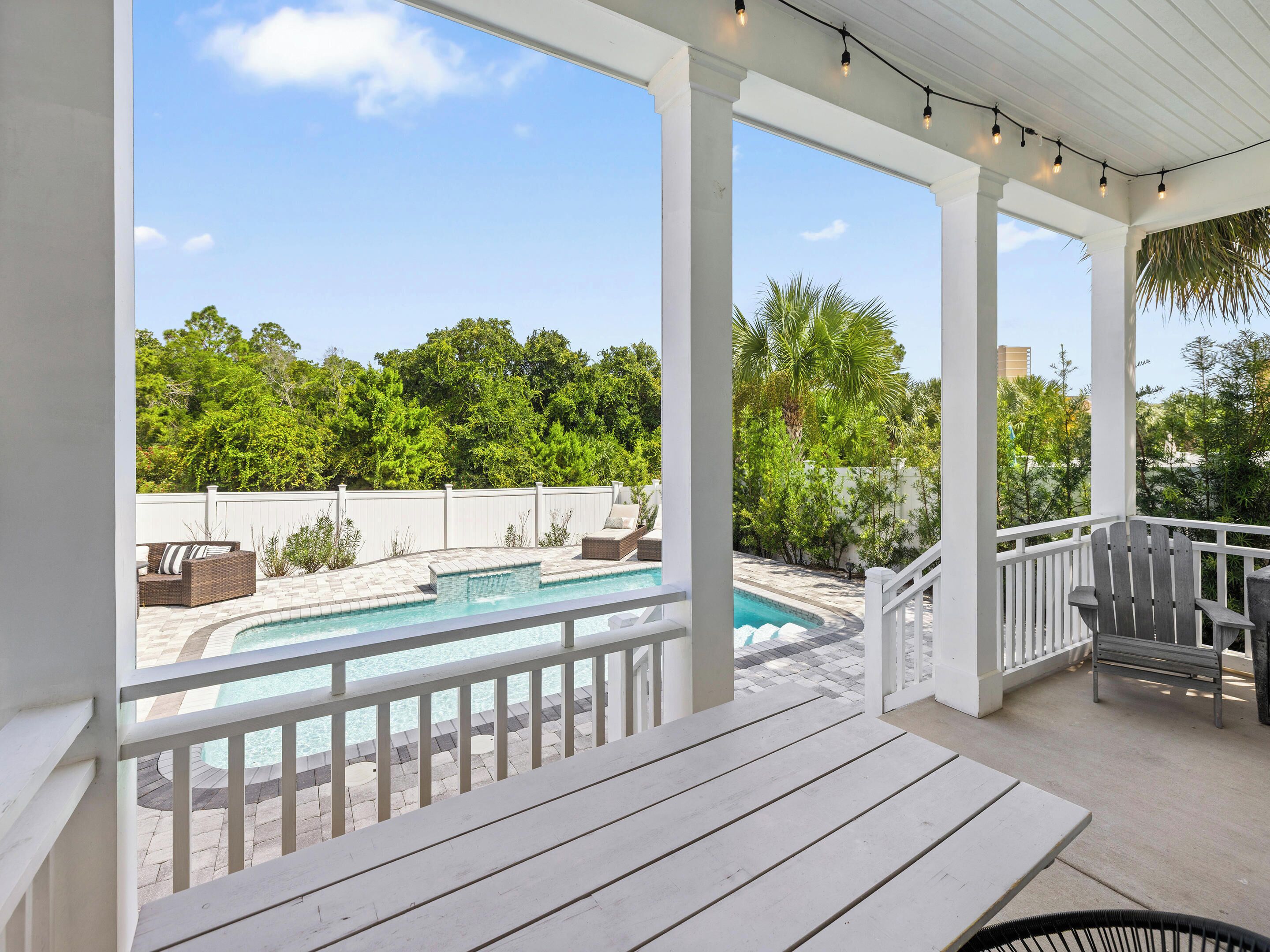 A covered outdoor area with a pool, white railings, and seating.