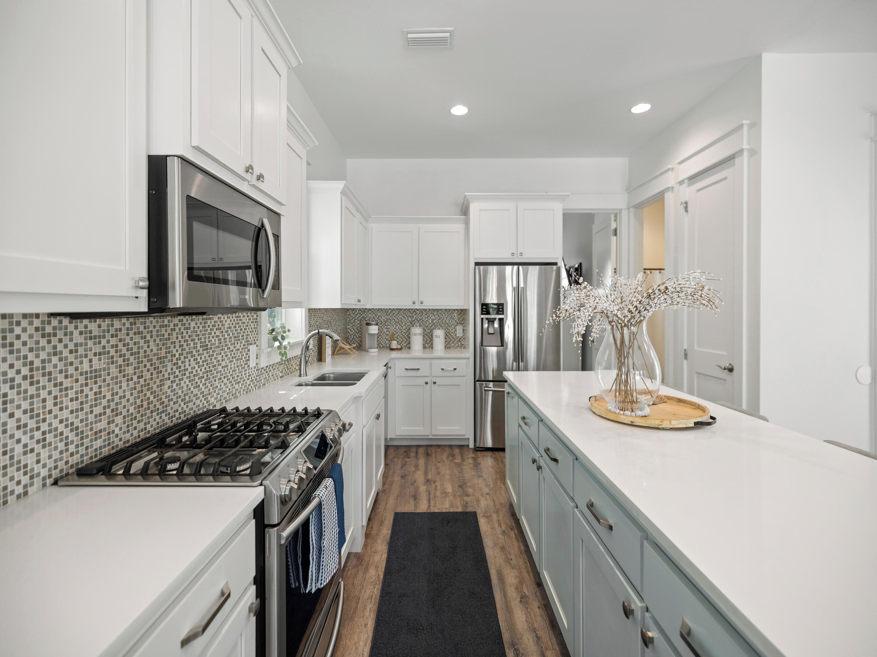 A modern kitchen with white cabinets, stainless steel appliances, a tiled backsplash, and a wooden floor.