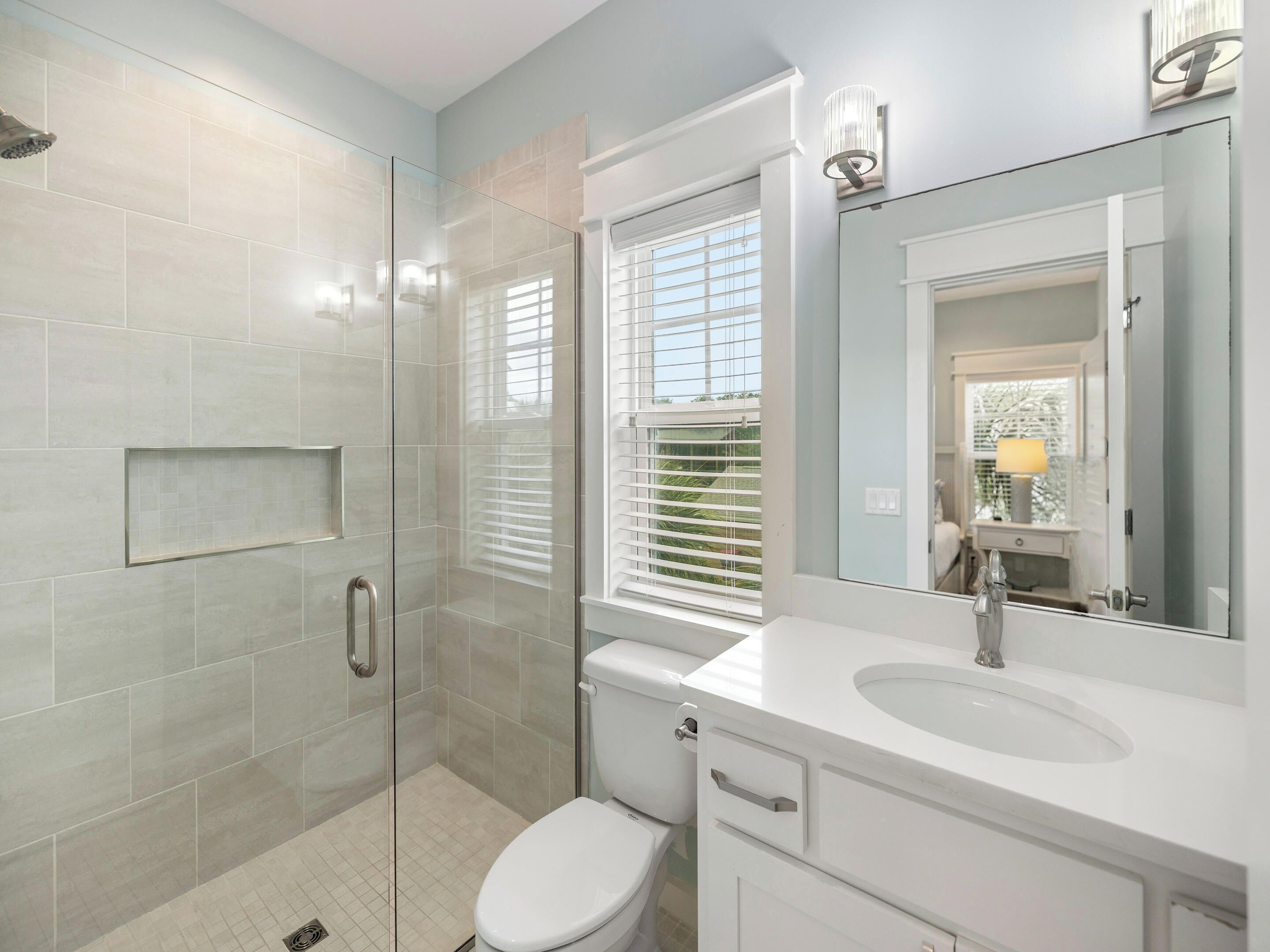 A modern bathroom with a glass-enclosed shower, a toilet, and a sink with a mirror above it.