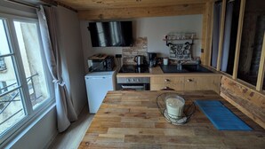 A compact kitchen with wooden cabinets, a microwave, a coffee maker, and a TV mounted above the counter. - La Darbella (Dole)