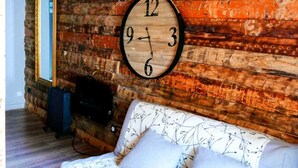 A rustic room with a wooden ceiling, a round wall clock, a sofa with floral upholstery, and a radiator against a brick wall. - La Darbella (Dole)